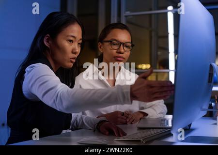 Ethnically diverse programmers working together on code at workplace in IT company office late in evening Stock Photo