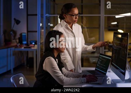 Ethnically diverse female programmers fixing code at night in modern office Stock Photo