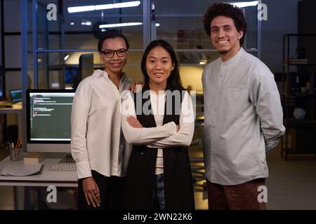 Portrait of successful ethnically diverse programmers posing for camera at workplace in IT company office late in evening Stock Photo