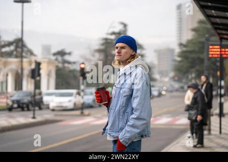 Pensive stylish trendy hipster guy with coffee looking into distance, waiting for taxi, girlfriend Stock Photo