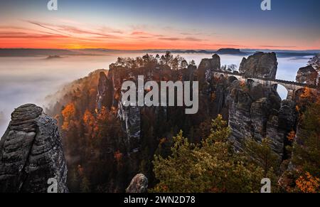 Saxon, Germany - Panoramic view of the Bastei bridge on a sunny autumn sunrise with colorful foliage and heavy fog under the hill. Bastei is famous fo Stock Photo