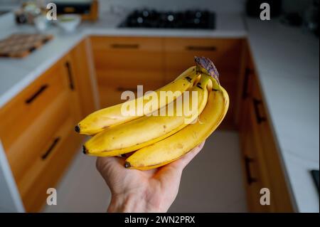 Man's hand holding bananas, natural daylight in the wooden kitchen Stock Photo