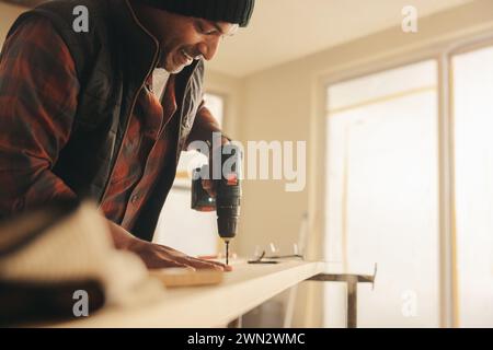Happy man using a power drill to secure a plank for baseboards in a home interior. Mature man renovating and refurbishing his kitchen using his self-t Stock Photo