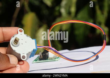 Stepper motor held in the hand that is used in many prototyping projects connected to a motor driver on the background Stock Photo
