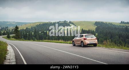 winding road in Carpathian mountains. Cloudy rainy weather in summer. Beige colored SEAT hatchback parked on the side of the mountain road. Stock Photo