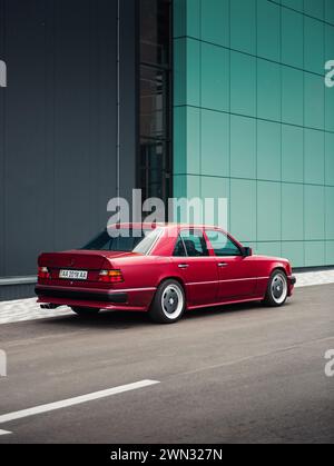 Rear three quarter view of Mercedes-Benz 400E (W124) in AMG body kit in front of turquoise wall. 1980s german sedan parked near modern building. Stock Photo