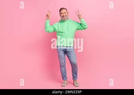 Full length photo of handsome senior man show double v-sign dressed stylish green garment isolated on pink color background Stock Photo