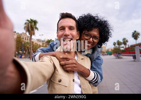 Happy multiracial middle-aged couple smiling at the camera while taking a selfie outdoors. Stock Photo