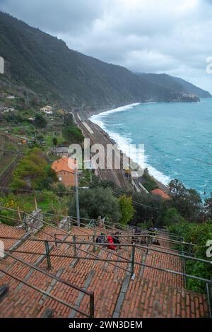 Cinque Terre, Italy–Jan 03, 2024: Tourists climbing up the stairs from train station to Riomaggiore with mountain and seashore Stock Photo