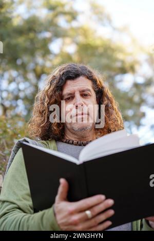 A mid adult man reading outdoors. Curly hair hairstyle Stock Photo