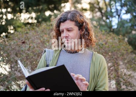 Handsome curly hair mature man reading book in the park. World book day Stock Photo