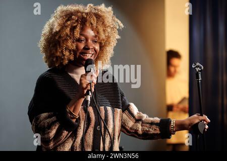 Happy young actress or comedian speaking in microphone while standing on stage in front of audience and performing new monologue Stock Photo