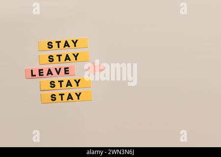 A set of yellow sticky notes present a conceptual decision-making scenario with the words stay and leave written on them Stock Photo