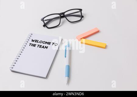 A white desk setup showcasing a notebook with Welcome to the team written on it, blue pen, black glasses, highlighters, symbolizing job opportunity an Stock Photo
