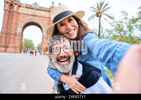 a man is carrying a woman on his back while they take a selfie Stock Photo
