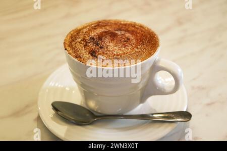 Cup of mouthwatering frothy cappuccino coffee on white table Stock Photo