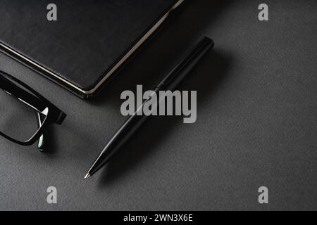 Top view of ballpoint pen, glasses and notepad lying on dark gray table Stock Photo
