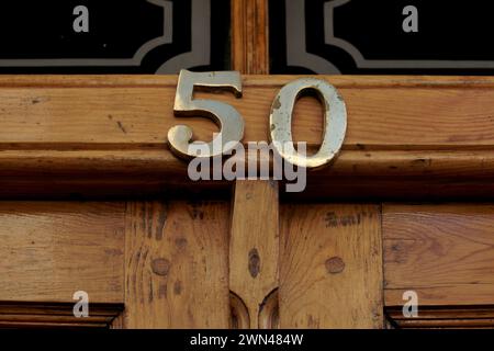 House number 50 with the fifty in bronze on a black wooden front door with panels edged in gold Stock Photo