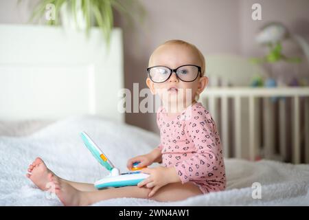 Toddler with glasses playing with an educational toy on a bed Stock Photo