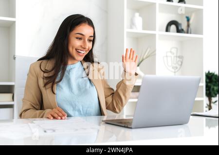 Video call. Positive successful indian or arabian business lady, company employee, sits in a modern office, using laptop for online video conference with business team or clients, greeting, smile Stock Photo
