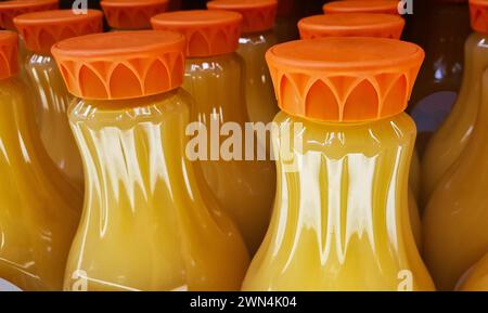 Orange juice bottles on a supermarket shelf with focus on foreground. Close up image, partial containers and lids shown. Stock Photo