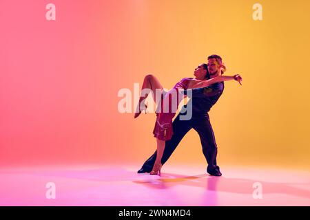 Young couple, man and woman in motion, ballroom dancers making creative performance against gradient pink yellow background in neon light Stock Photo