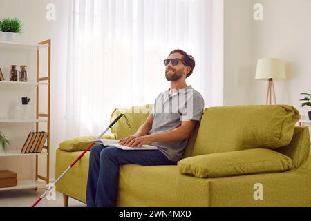 Blind Man Smiles While Reading Braille Book on Sofa Stock Photo