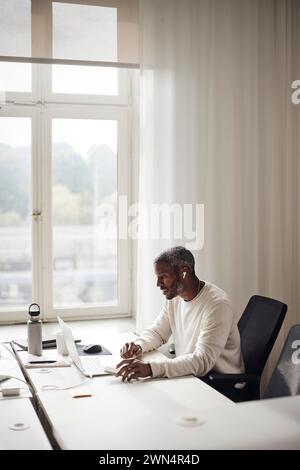 Businessman working on laptop at desk while sitting in office Stock Photo