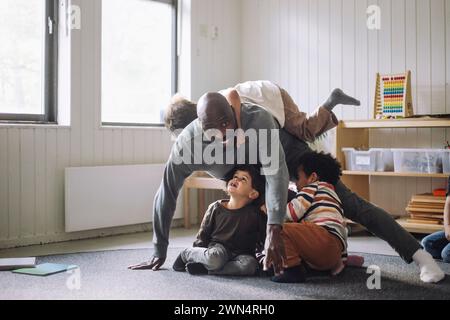 Smiling male teacher having fun while playing with kids in classroom at kindergarten Stock Photo