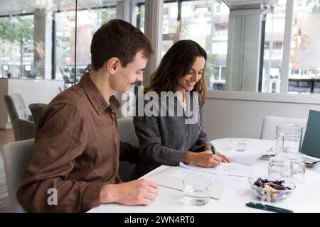 Man looking at woman smiling while signing agreement at desk in real estate office Stock Photo