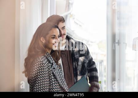 Smiling multiracial couple looking through window in balcony while exploring new house Stock Photo