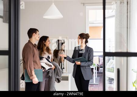 Saleswoman talking with happy male and female clients during house visit Stock Photo