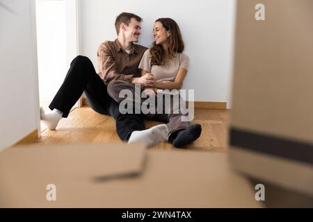 Happy multiracial couple with hands intertwined sitting on hardwood floor at home Stock Photo