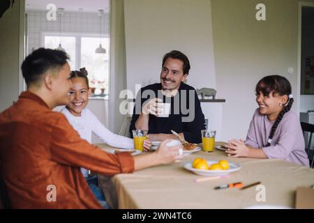 Happy gay couple spending leisure time with daughters while having breakfast at dining table in home Stock Photo