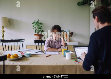 Girl studying with father using laptop while sitting at dining table in home Stock Photo