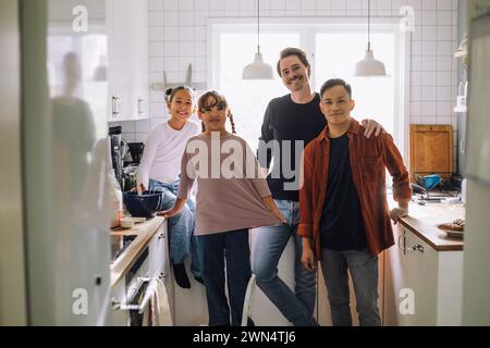 Portrait of happy gay men standing with daughters in kitchen at home Stock Photo