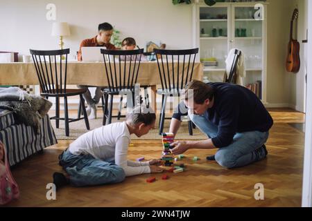 Father teaching daughter to play Jenga while sitting on floor at home Stock Photo