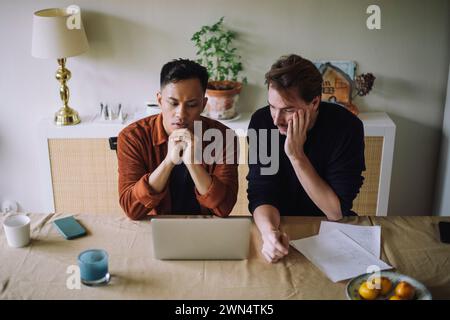 High angle view of worried gay couple sitting with laptop on table at home Stock Photo