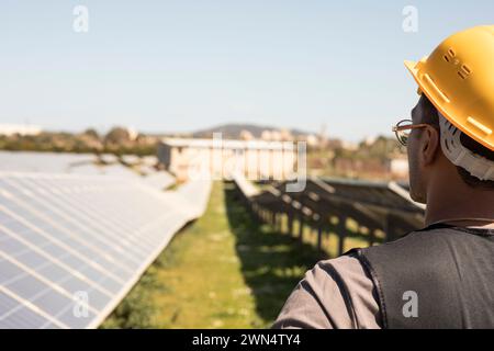 Male engineer wearing hardhat while looking at solar panels in field Stock Photo