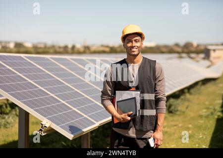 Portrait of smiling male engineer holding documents and digital tablet while standing near solar panels at power station Stock Photo
