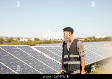 Young male engineer wearing reflective jacket while looking at solar panels at power station Stock Photo