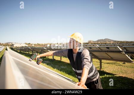 Young male engineer drilling while working near solar panels at power station Stock Photo