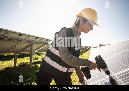 Female engineer using drill while working near solar panels at power station Stock Photo