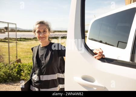 Portrait of smiling senior female engineer standing next to van at power station Stock Photo