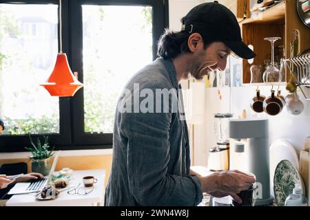 Side view of smiling male architect preparing coffee while standing in kitchen at home office Stock Photo
