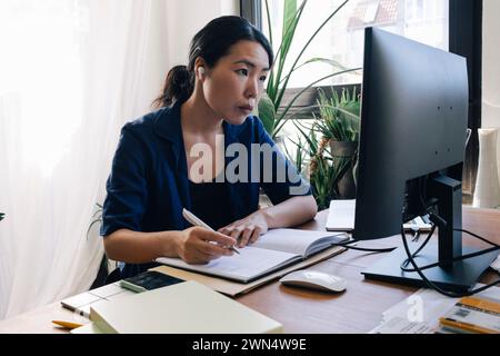 Confident female architect with diary looking at computer monitor on desk in home office Stock Photo
