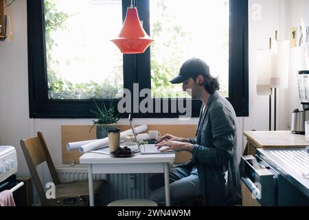 Side view of male architect using laptop at desk in home office Stock Photo