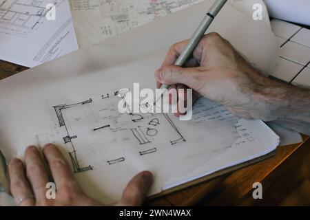 Cropped hands of male architect sketching blueprint on paper at desk in home office Stock Photo