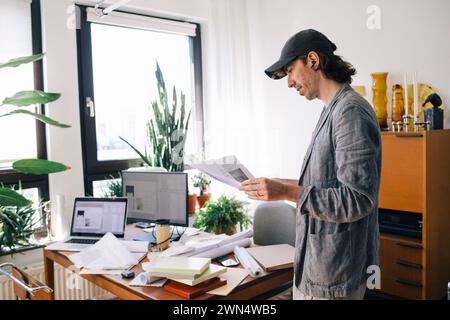 Side view of male architect analyzing blueprint while standing by desk in home office Stock Photo