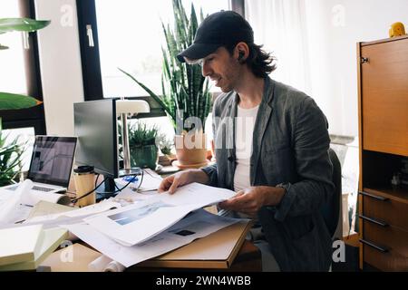 Male architect analyzing blueprint while sitting at desk in home office Stock Photo